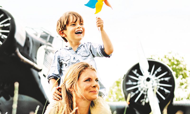 Eine Mutter mit ihrem Sohn vor einem Flugzeug, beide lachen glücklich